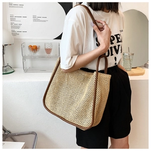 Detailed side view of a large straw tote bag with brown leather trim worn by a model