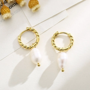 Baroque style gold twisted hoop earrings with white pearl pendants on white textured paper