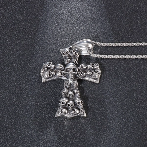 Close-up of a silver stainless steel cross pendant with detailed skull relief and rope chain