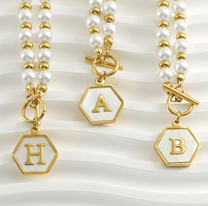 Détail de bracelets en perles dorées avec pendentifs hexagonaux aux initiales A B H