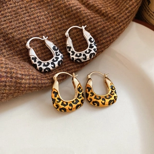 Detail shot of leopard print U-shaped earrings in gold and silver on a textured surface