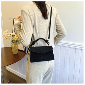 Detailed view of black suede shoulder bag with dual straps shown in minimalist setting
