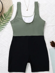 Detail view of a color-block one-piece swimsuit with olive top and black shorts on a beach set