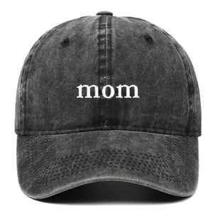 Close-up of white 'mom' embroidery on a washed charcoal grey cotton baseball cap
