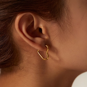 Golden heart-shaped stainless steel hoop earrings worn on a model's ear for style