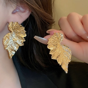 Elegant gold leaf earrings with textured metal veins worn by a fashion model