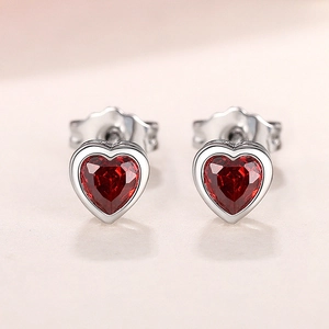 Macro shot of silver heart earrings with faceted red gemstones and secure butterfly backs