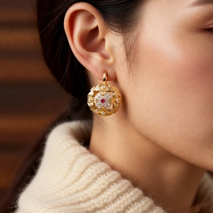 Close-up of vintage golden hollowed-out earring with a red gemstone and tiny diamonds