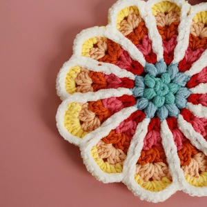 Handmade crochet flower coaster with vibrant gradient yarn colors on pink background