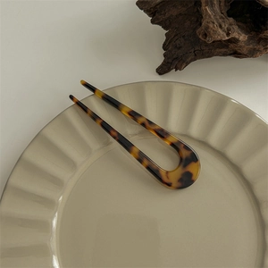 Detail of tortoise shell resin U-shaped hair pin on a ceramic plate for vintage styling