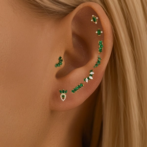 Close-up of gold diamond flower stud earrings with green zircon on a model's ear