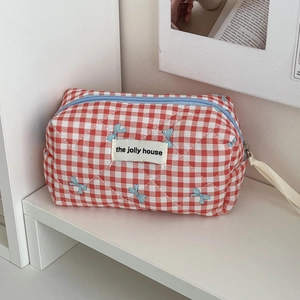 Detail of red checkered quilted makeup bag with blue bow pattern and blue zipper closure