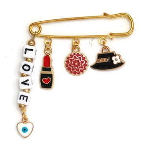 Detailed close-up of gold safety pin brooch with enamel lipstick, flower, and heart charms