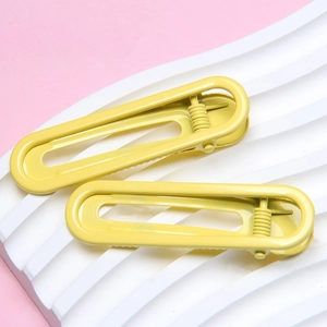 Detail of bright yellow metal U-shaped hair clips on white wavy tray background