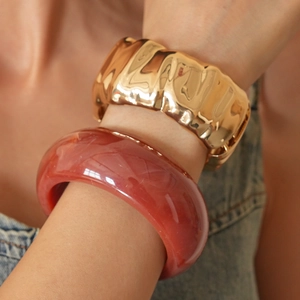 Detail of red translucent resin and hammered gold metal bangle bracelets set on wrist