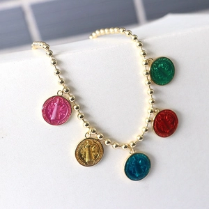 Macro view of gold beaded bracelet featuring five colorful Saint Benedict medal charms