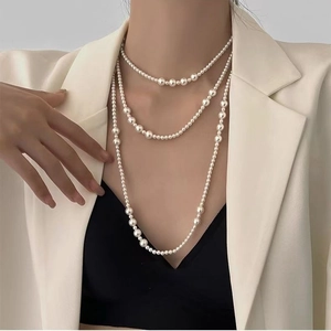 Detail of layered white pearl necklace with opal pendant worn by a model in a beige suit