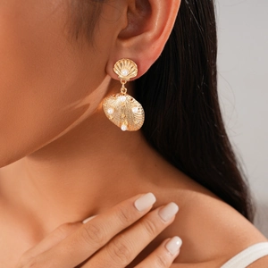Close-up of golden shell-shaped earring with pearl worn by a model for a beach style