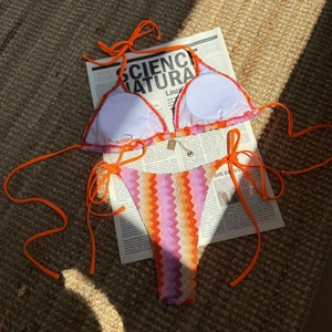 Detail of striped knit bikini with gold heart pendant on textured brown background