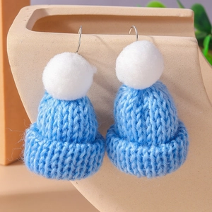 Close-up of blue knitted hat earrings with white pompom and silver hooks