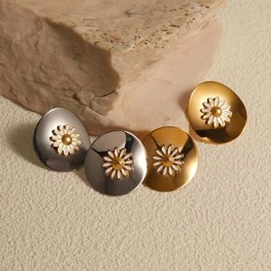 Detail view of gold and silver bowl-shaped stud earrings with white daisy flower motifs