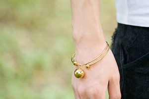 Detail of a gold double-layer bangle featuring three spherical charms on a woman's wrist