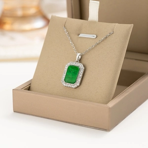 Close-up of a silver necklace with a green rectangular gemstone and halo diamonds