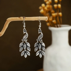 Detailed view of silver peacock earrings with tassels on a wooden stand in retro style