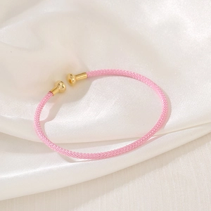 Pink woven mesh bracelet with gold cylindrical ends on elegant white silk fabric