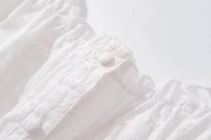 Close-up of white lace dress with floral embroidery, fabric buttons and ruffle details