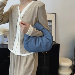 Minimalist blue denim dumpling bag with knot handle carried by model in casual outfit