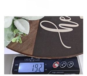 Detail showing wood door sign weight of 192g with green foliage on digital scale