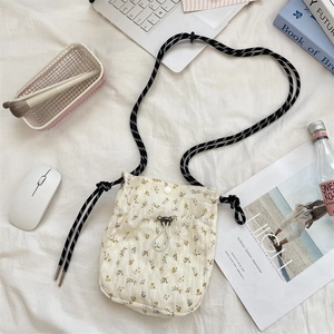 Detailed close-up of a floral canvas crossbody bag with woven strap on a soft white bed