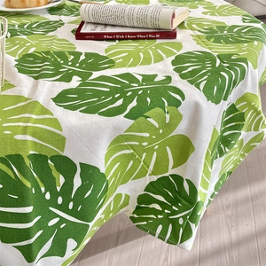 Detail of linen tablecloth with green monstera leaf pattern on white fabric