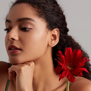 Detailed view of rose gold dachshund stud earrings worn by a model with red flowers