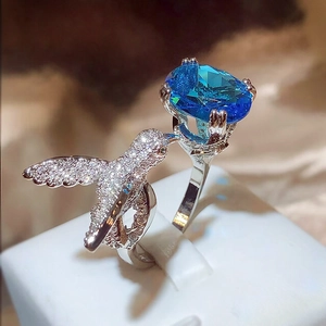 Macro shot of a hummingbird ring with a large oval blue gemstone and diamond pavé details