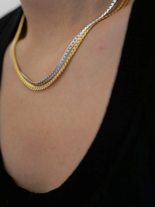 Close-up of stacked gold and silver herringbone chains on a dark shirt background