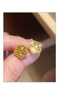Makroaufnahme goldener Ohrstecker in Blütenform mit matter Textur und Perlenrand-Design