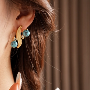 Macro shot of S-shaped vintage earrings with blue turquoise and diamonds on model