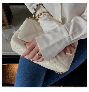 Detail of a beige quilted leather shoulder bag with a chunky gold metal chain handle