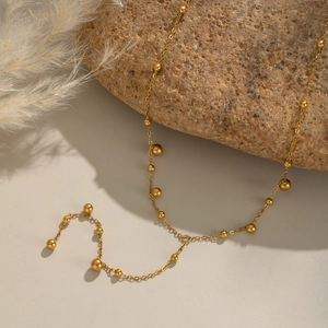 Detailed view of gold 18K plated stainless steel Y-necklace with ball pendants on a stone
