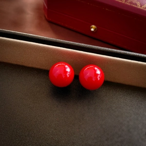 Macro shot of minimalist high-gloss red spherical stud earrings on dark textured surface
