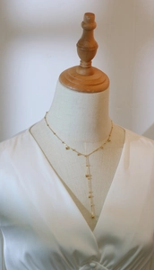 Detail of 18K gold-plated Y-shaped tassel necklace with gold beads on a silk background