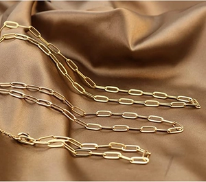 Macro detail of a gold-plated paperclip chain necklace on premium brown silk fabric