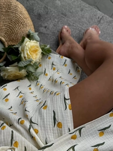 Detail of white cotton floral dress with yellow tulip prints and textured woven straw bag