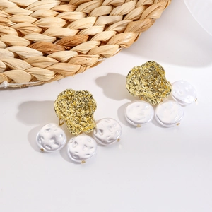 Detail of bohemian gold hammered metal earrings with three baroque pearls on a woven mat