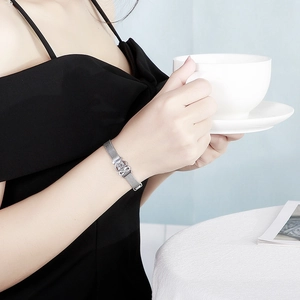 Close-up of silver mesh bracelet with crown buckle on a model holding a coffee cup