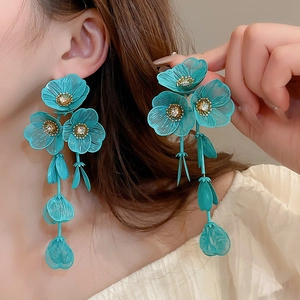Detail of teal flower petal earrings with metallic texture and long tassel fringe