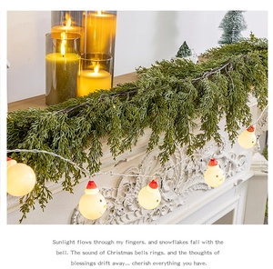 Detailed view of artificial cypress garland with warm LED snowman lights on a mantel