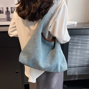 Blue denim tote bag with brown leather straps shown on a model in a minimalist setting